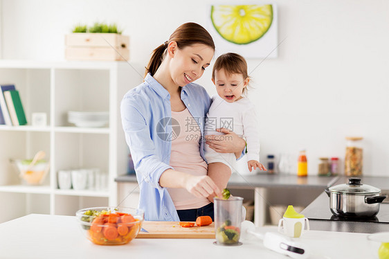 家庭,食物,健康的饮食,烹饪人们的快乐的母亲添加切碎的蔬菜搅拌机杯抱着小女孩家里的厨房快乐的母亲婴儿家厨房图片