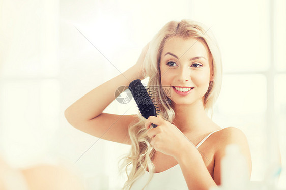美丽,修饰人的微笑的轻女人看着镜子,家里的浴室用梳子梳头快乐的女人浴室用梳子刷头发快乐的女人浴室用梳子刷图片