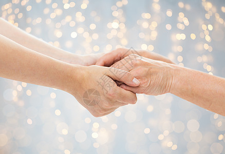 龄,护理支持亲密的老妇女轻妇女牵手的假日灯光背景亲密的老人轻的女人牵手图片