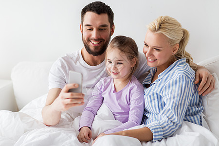 人,家庭技术的快乐的母亲,父亲小女孩家里用智能手机自拍幸福的家庭家里用智能手机自拍图片