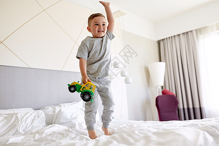 人,童早晨的快乐的小男孩与玩具汽车家里酒店床上快乐的小男孩,玩具车家里酒店床上背景图片
