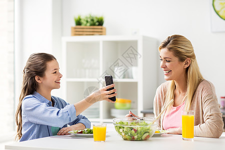 家庭,技术人的快乐的母亲女儿与智能手机家里的厨房吃饭智能手机的幸福家庭家吃饭图片