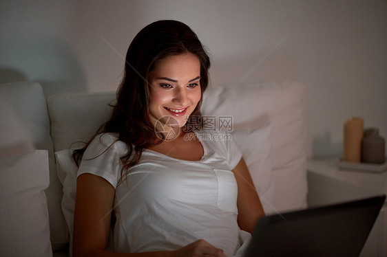 技术,互联网,沟通人的快乐的微笑轻妇女与笔记本电脑床上家里的卧室晚上快乐的女人家里卧室的床上笔记本电脑图片