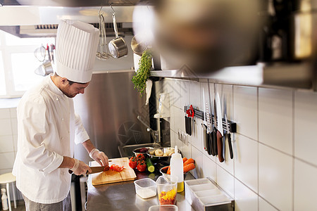 烹饪食物,职业人的快乐的男厨师用刀切西红柿餐厅厨房的砧板上饭快乐的男厨师餐厅厨房烹饪食物图片