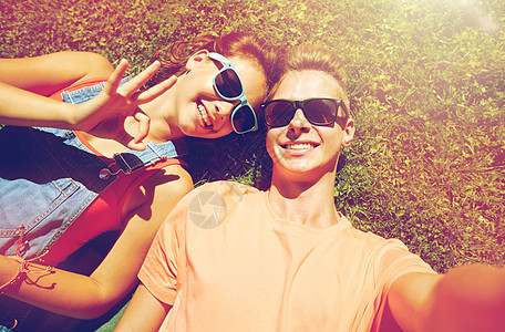 爱人的快乐的青少夫妇戴着太阳镜躺草地上,夏天自拍快乐的十几岁的夫妇夏天的草地上自拍图片