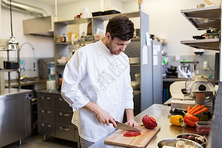 烹饪食物,职业人的快乐的男厨师用刀切辣椒餐厅厨房的砧板上快乐的男厨师餐厅厨房烹饪食物图片