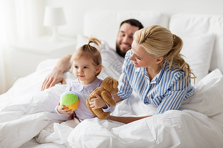 人,家庭早晨的快乐的孩子与玩具父母床上家快乐的孩子带着玩具父母家里睡觉图片