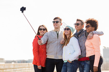 人,友谊技术群微笑的十几岁的朋友户外用智能手机自拍杆拍照快乐的朋友户外用智能手机自拍图片