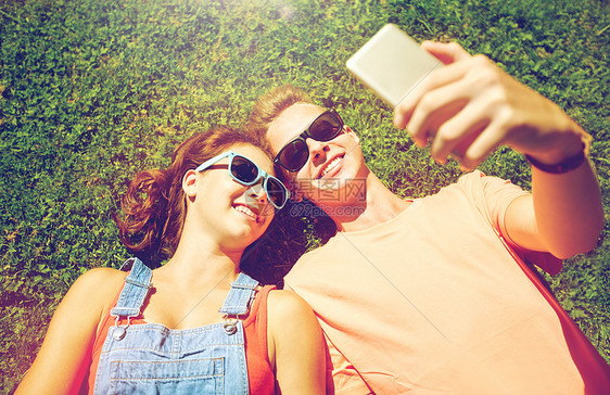 爱人的快乐的青少夫妇戴着太阳镜躺草地上,夏天智能手机上自拍快乐的夫妇夏天智能手机上自拍图片