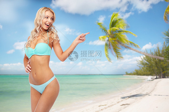 人们,旅行暑假的快乐微笑的轻女人穿着比基尼泳衣指着异国情调的热带海滩与棕榈树的背景快乐微笑的轻女人穿着比基尼海图片