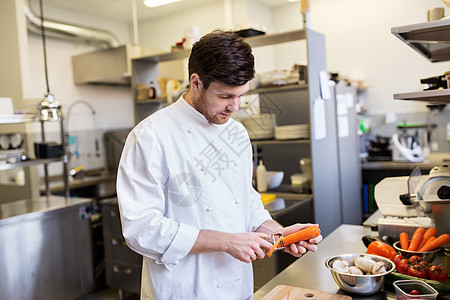 烹饪食物,职业人的快乐的男厨师用刀削胡萝卜餐厅厨房的砧板上饭快乐的男厨师餐厅厨房烹饪食物图片