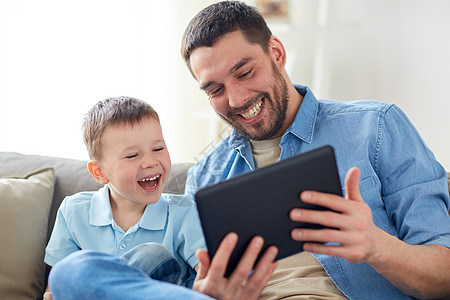 家庭,父亲,技术人的快乐的父亲小儿子坐沙发上的平板电脑电脑家父子俩家里玩平板电脑图片