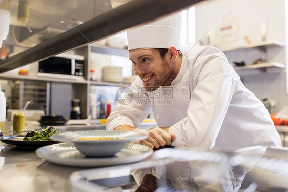 食物烹饪,职业人的快乐的男厨师烹饪与盘子汤沙拉餐厅厨房桌子快乐的男厨师餐厅厨房烹饪食物图片