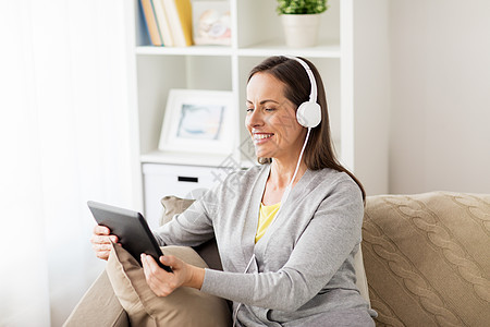 人技术休闲理念快乐的女人坐沙发上,用平板电脑耳机家听音乐家里平板电脑耳机的快乐女人图片