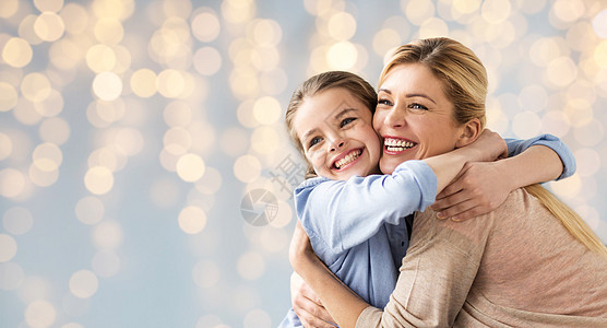 微笑日人家庭的快乐的微笑女孩与母亲拥抱节日的灯光背景快乐的女孩母亲拥抱灯光背景