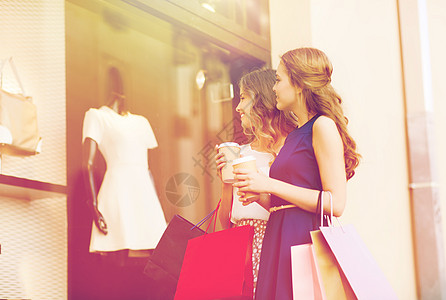 销售,消费主义人的快乐的轻妇女,购物袋咖啡纸杯看着商店的窗口户外轻的女人商店里着购物袋咖啡背景图片