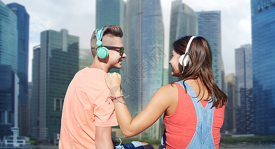 技术,爱人的快乐的青少夫妇戴着耳机,新加坡城市摩天大楼的背景上听音乐十几岁的夫妇戴着耳机河边图片