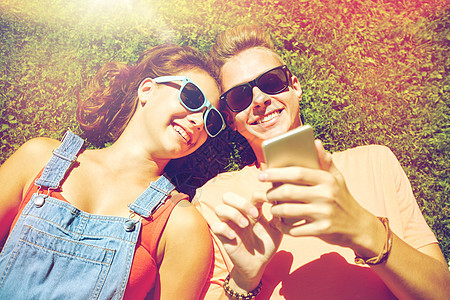 爱人的快乐的青少夫妇戴着太阳镜,智能手机躺草地上夏天快乐的十几岁的情侣智能手机躺草地上图片