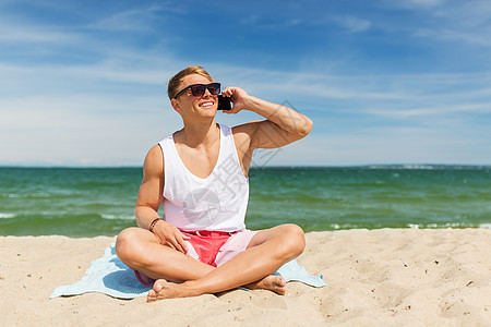 暑假人们的快乐的微笑轻人戴着太阳镜,海滩上打电话给智能手机微笑的男人夏天的海滩上打电话给智能手机图片