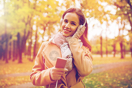 季节,技术人的美丽的快乐轻女子戴着耳机,智能手机上听音乐,秋天的公园散步秋天公园里智能手机耳机的女人图片