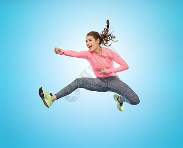 运动,健身,运动人的快乐的轻女人空中跳跃,蓝色背景上的战斗姿势快乐运动的轻女人跳战斗姿势图片