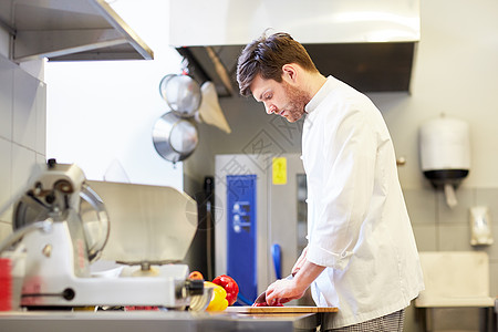 烹饪食物,职业人的快乐的男厨师用刀切辣椒餐厅厨房的砧板上快乐的男厨师餐厅厨房烹饪食物背景图片