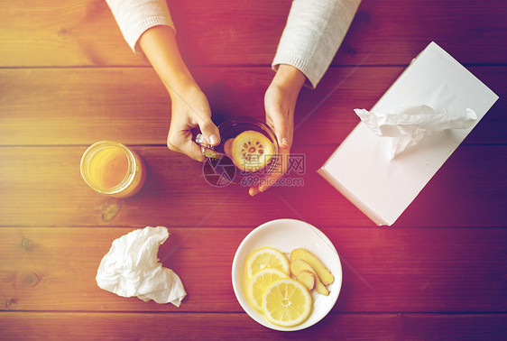 健康,传统医学民族科学生病的女人喝茶与柠檬,蜂蜜生姜纸巾盒木桌上生病的女人喝柠檬生姜的茶图片
