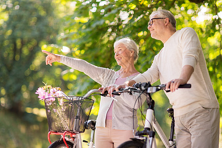 自行车背景老人,人生活方式的快乐的老夫妇步行与固定自行车夏季城市公园快乐的老夫妇夏季公园骑自行车背景