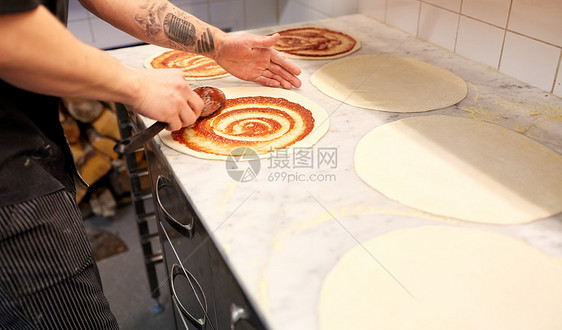 食物烹饪,烹饪人们的烹饪包师用勺子涂番茄酱比萨生披萨店用番茄酱披萨图片