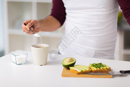 饮食,人饮食男人茶咖啡杯中添加糖,并家庭厨房早餐吃蔬菜三明治男人吃早餐,咖啡中加糖图片