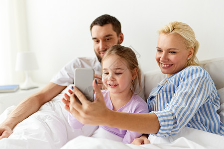 父亲小女孩家里的床上智能手机家里智能手机的幸福家庭图片