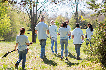 志愿服务慈善人生态群快乐的志愿者,他们带着树苗花园工具公园里散步幼苗花园工具的快乐志愿者图片