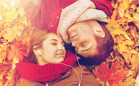 北京秋天爱,关系,季节,家庭人的亲密的幸福夫妇与耳机听音乐躺秋天的树叶上靠近躺秋天公园里微笑的夫妇背景