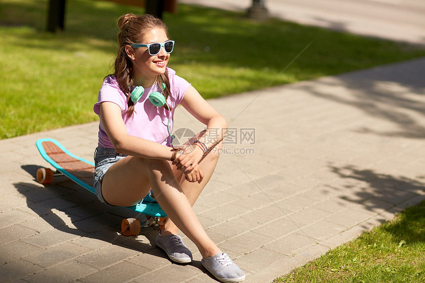 生活方式,休闲人们的微笑的轻妇女十几岁的女孩戴着太阳镜,戴着耳机坐公园的长板上带耳机长板的快乐少女图片