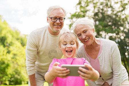 家庭世代人的快乐的微笑祖母,祖父小孙女公园用智能手机自拍祖父母孙女自拍图片