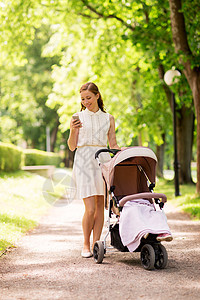 母亲,技术人的快乐的母亲与智能手机女婴婴儿车夏季公园快乐的母亲公园用智能手机婴儿车图片