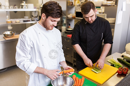 烹饪食物,职业人的快乐的男厨师用刀削胡萝卜切黄瓜餐厅厨房的砧板上厨师烹饪食物餐厅厨房图片