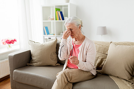 老,健康问题,视力人的老妇女戴着眼镜坐沙发上,家头痛戴眼镜的老妇女家头痛图片