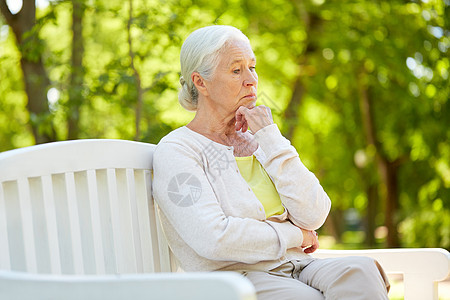 老,退休人们的悲伤的老妇女戴着眼镜,坐夏季公园的长凳上悲伤的高级女人坐夏天公园的长凳上图片