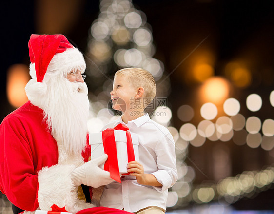 节日人的诞老人快乐的小男孩与礼品盒诞树灯光背景诞老人带诞礼物的快乐男孩图片
