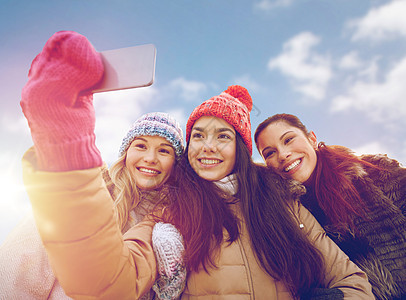 人,友谊,技术,冬季休闲快乐的十几岁女孩自拍与智能手机户外快乐的十几岁女孩用智能手机自拍图片