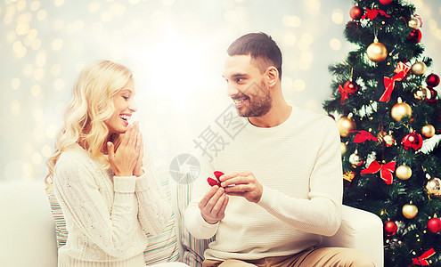 爱,夫妇,求婚人的快乐的男人小红盒子里给女人诞树灯光背景上的订婚戒指男人给女人诞订婚戒指图片