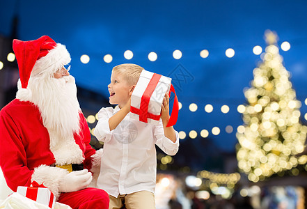 节日人的诞老人快乐的小男孩与礼品盒诞树灯光背景诞老人带诞礼物的快乐男孩图片