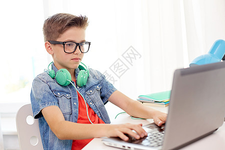 游戏笔记本技术,教育人的学生男孩戴着眼镜,戴着耳机家里的笔记本电脑上打字戴眼镜的学生家里用笔记本电脑打字背景