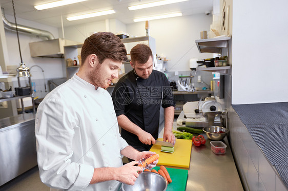 烹饪食物,职业人的快乐的男厨师用刀削胡萝卜切黄瓜餐厅厨房的砧板上厨师烹饪食物餐厅厨房图片