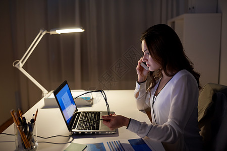 商业,技术,过度工作,截止日期人的女人带着笔记本电脑夜间办公室打电话给智能手机笔记本电脑的女人办公室打电话给智背景图片