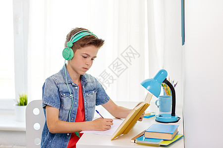 童享好音乐教育,童人的快乐的学生男孩戴着耳机,家里的书笔记本学生男孩戴着耳机写笔记本上背景