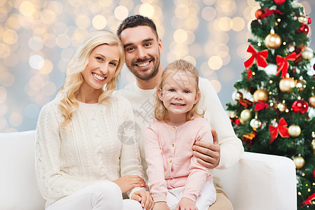 家庭,诞节,假日人的快乐的母亲,父亲小女儿坐沙发上的灯光背景诞树上的幸福家庭图片
