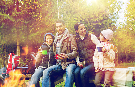 旅行,旅游,徒步旅行人们的幸福的家庭坐长凳上,喝着热茶杯子营地火灾树林快乐的家庭篝火上喝热茶图片