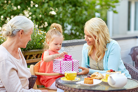 家庭世代人的快乐的祖母母亲咖啡馆餐馆露台给小女儿送礼物快乐的母亲咖啡馆给女儿送礼物图片